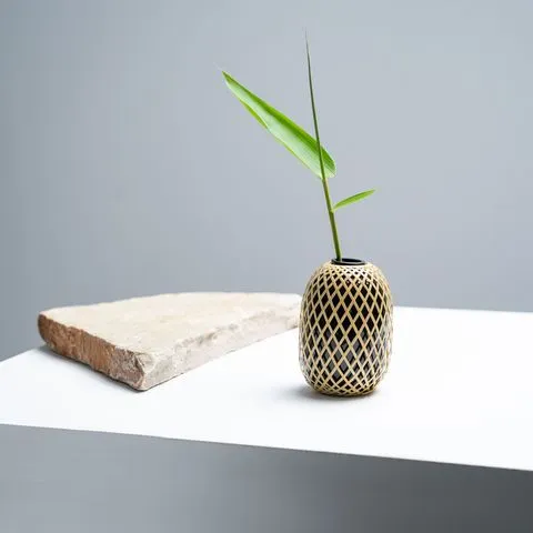 一個小型編織格紋花器與綠色植物置於白色檯面上,旁邊有一塊粗糙的長方形石板。